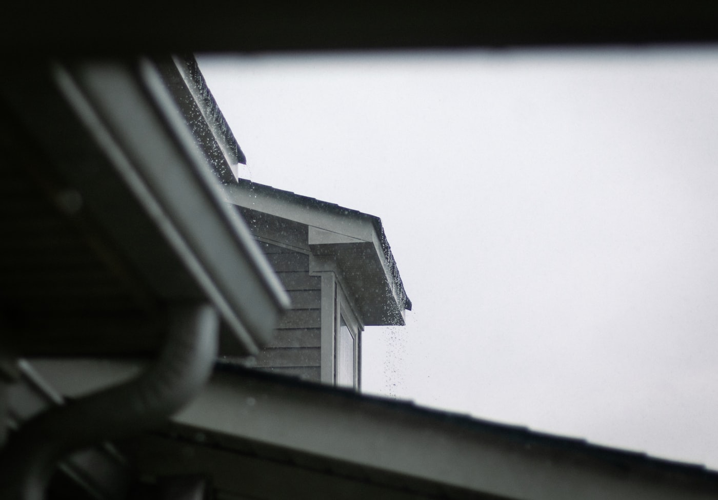Canaleta y bajada de aguas lluvias en el alero de una casa bajo cielo gris, instalación de canaletas en Chile